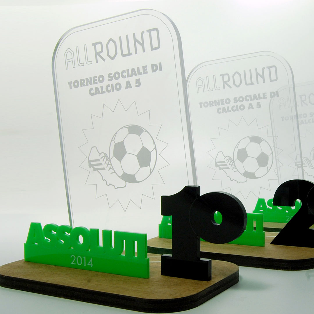 Piccoli trofei in plexiglass trasparente con incisioni palla da calcio e numeri in plexiglass colorato su base di legno.